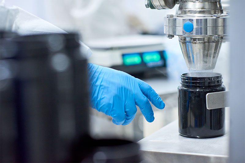 Factory employee filling jar from manufacturing order of sports supplement, creatine, hmb, bcaa, amino acid or powdered vitamin. Sports nutrition production