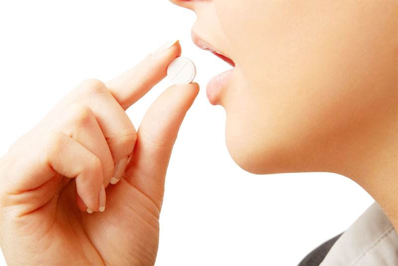 Close-up of a woman's hand holding a white dissolvable tablet near her mouth, ready to take a quick-melt tablet supplement.